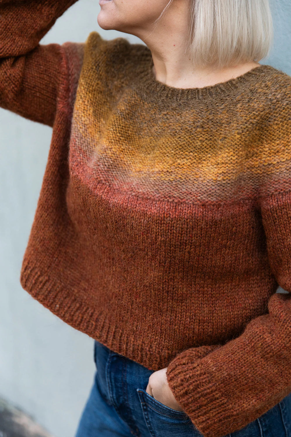 a white woman with short blonde hair wears a kitted sweater in brown, yellow, red, and maroon