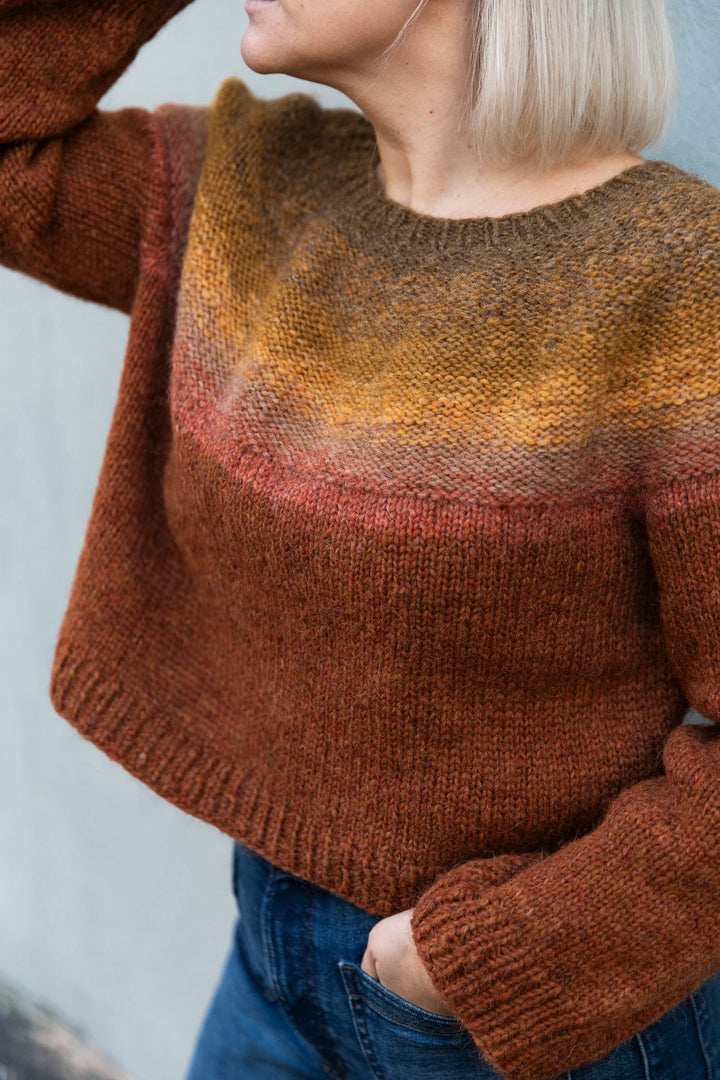 a white woman with short blonde hair wears a kitted sweater in brown, yellow, red, and maroon