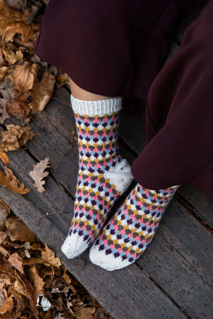 The legs  and feet of a person wearing dark purple pants and knitted socks with a variety of colors used.