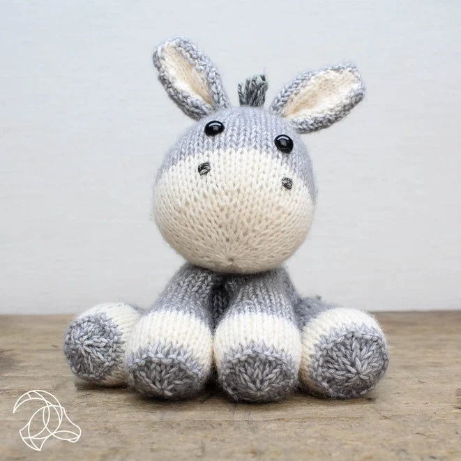Knitted donkey toy on a wooden surface with a light gray background