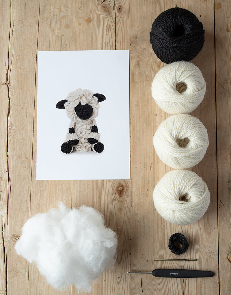 animal card, poly stuffing, balls of yarn, darning needle, and a crochet hook lying on a wooden table