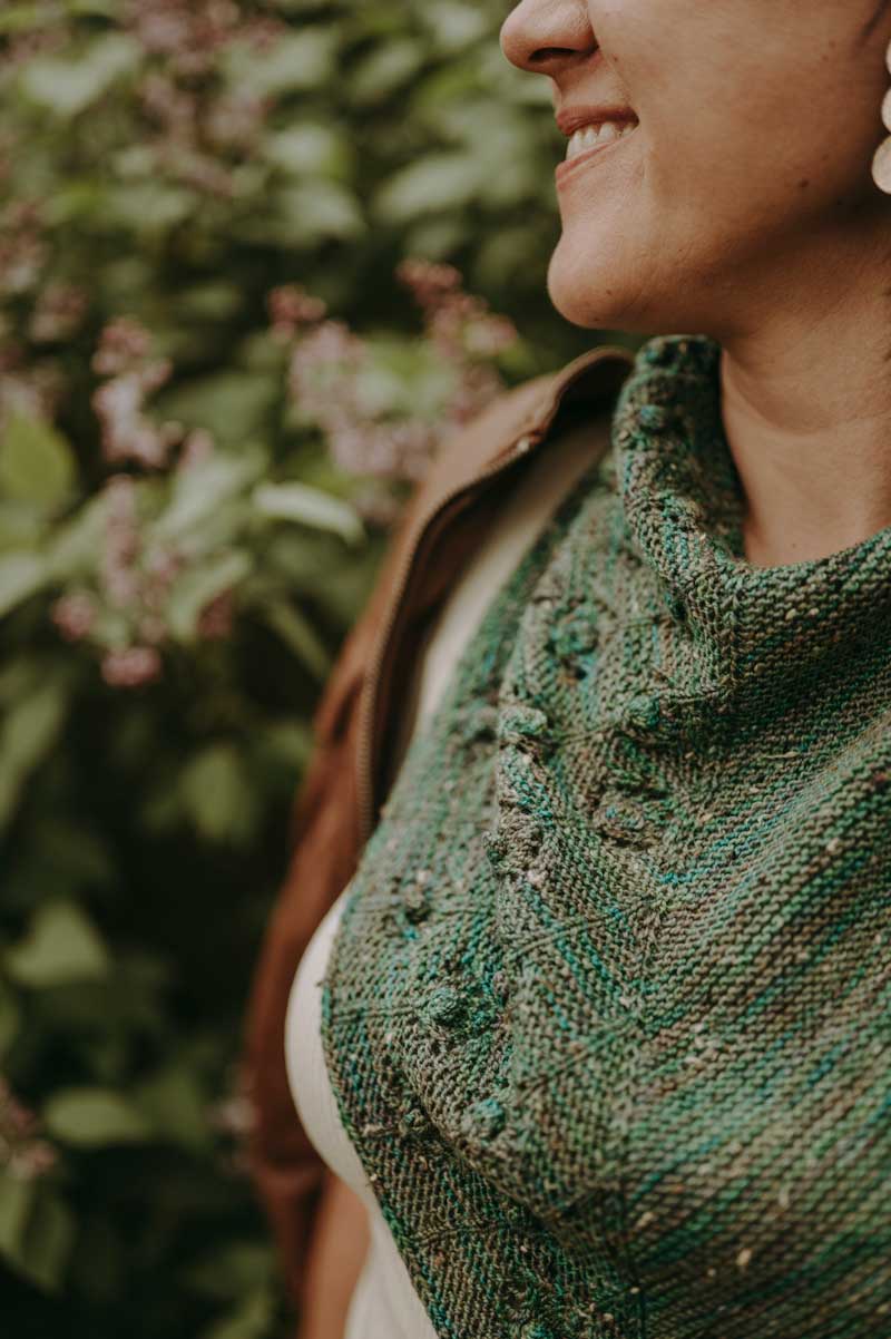 Person wearing a green knitted shawl with a blurred natural background