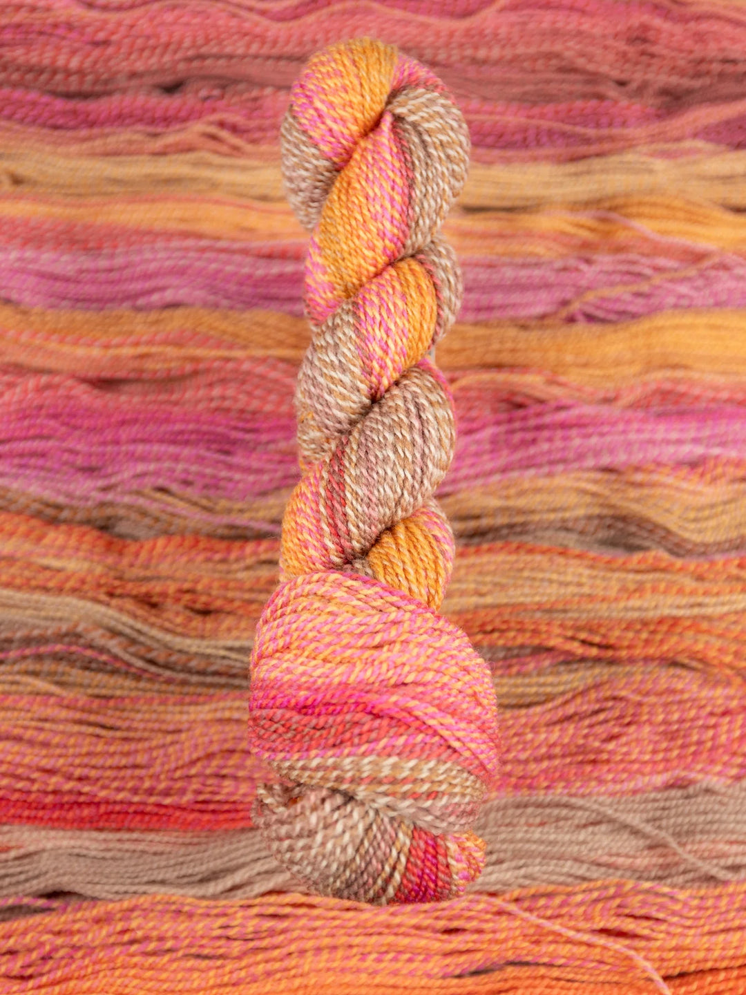 Colorful skein of yarn on a textured pink and orange fabric background