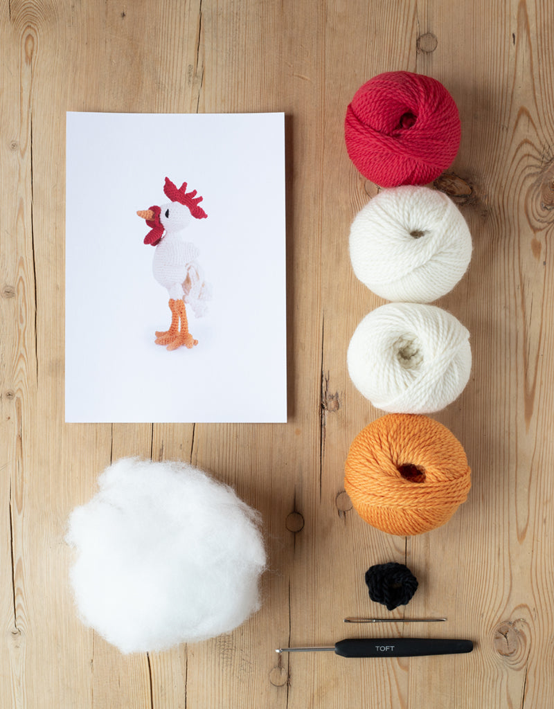 animal card, poly stuffing, balls of yarn, darning needle, and a crochet hook lying on a wooden table