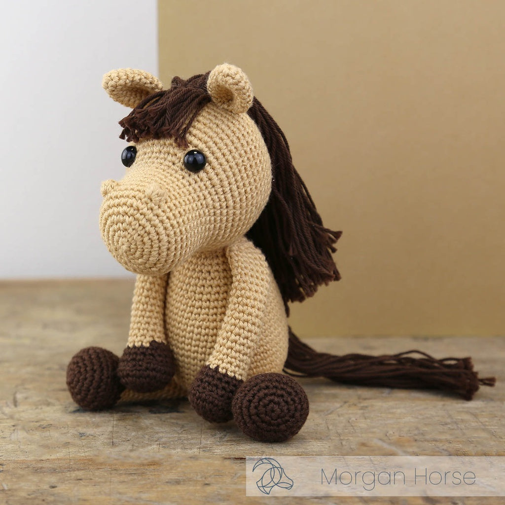 Crocheted horse toy with brown mane and feet on a wooden surface, brand 'Morgan Horse' visible.