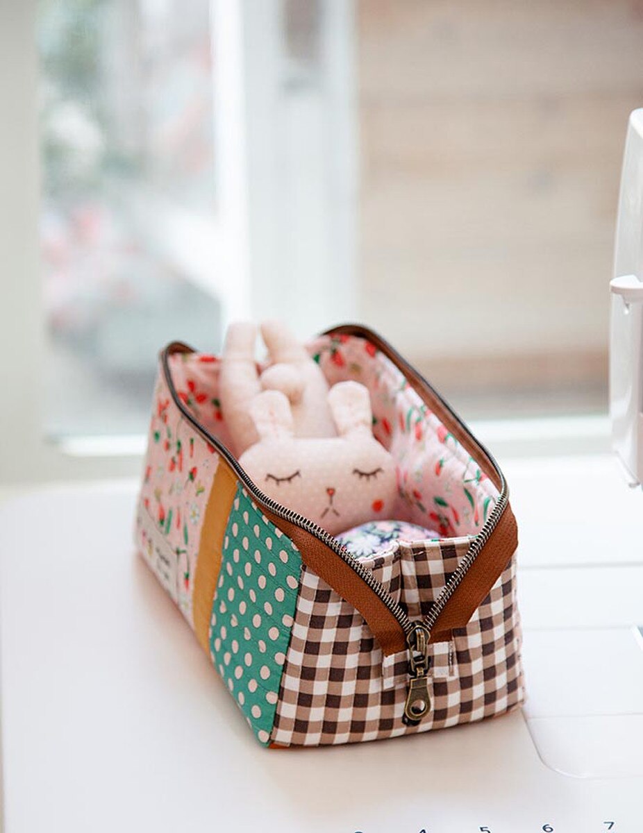 Patchwork-style fabric basket with a plush toy inside on a light surface.