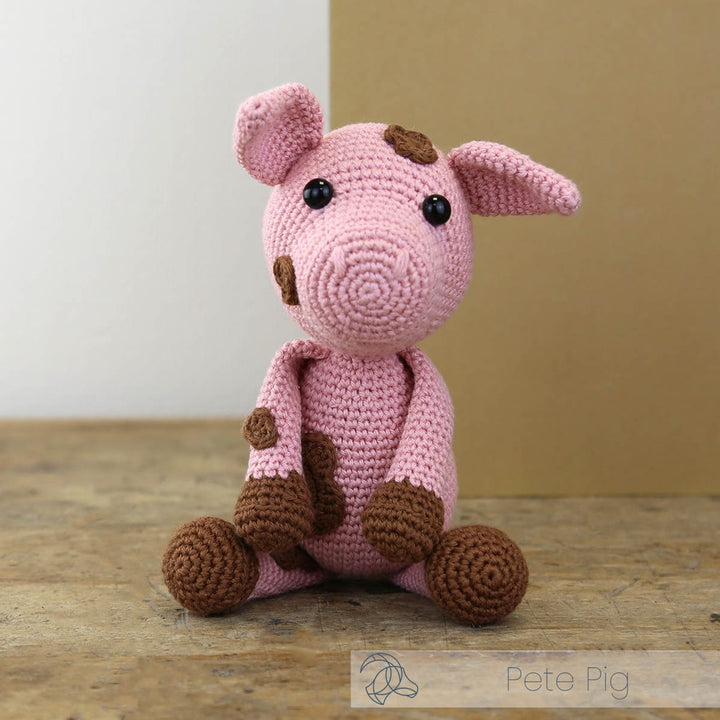 Crocheted pink pig toy with brown accents on a wooden surface