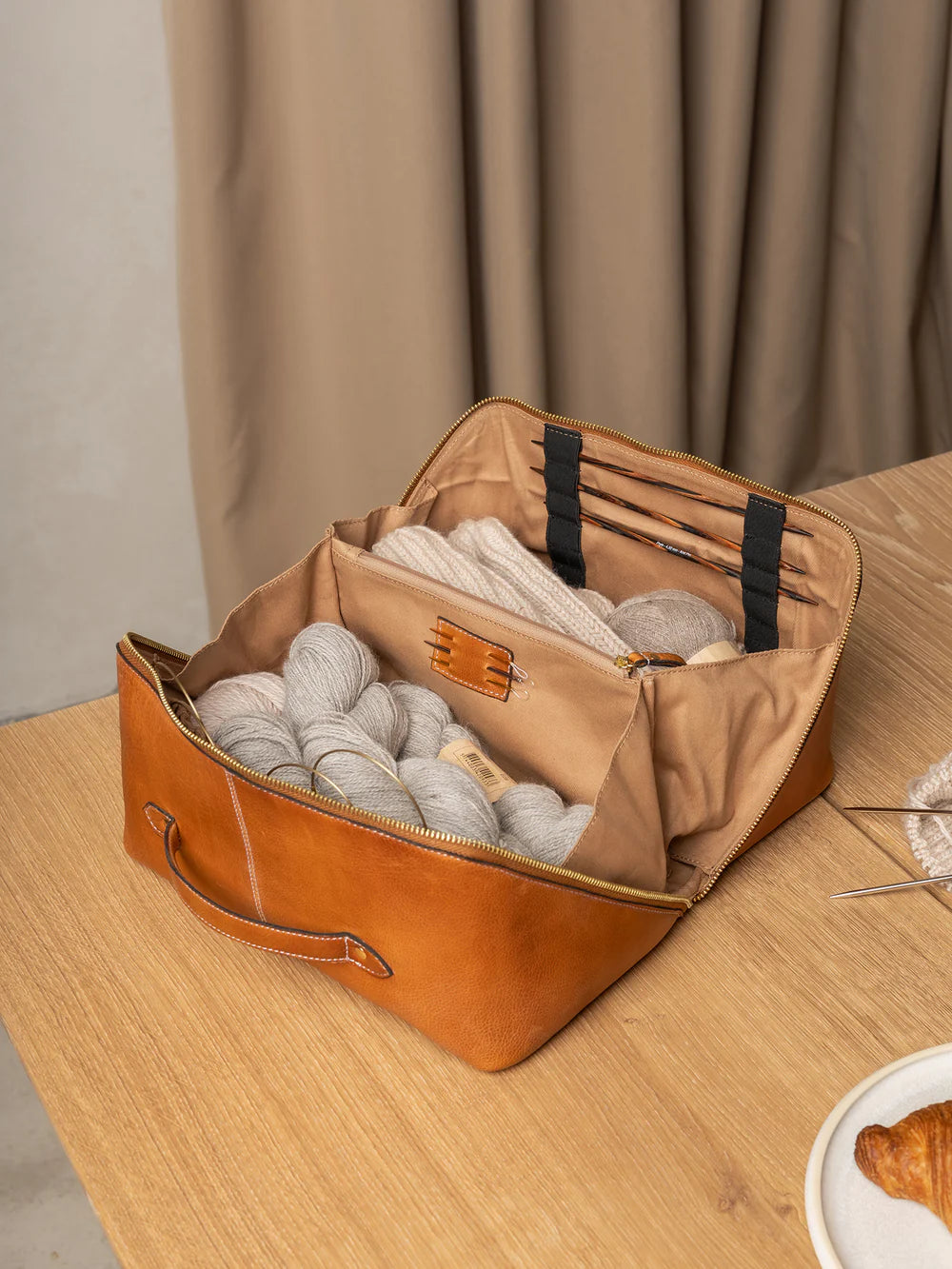 Brown leather bag with gray yarn balls on a wooden table