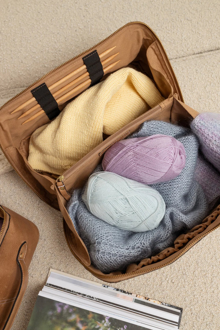 Open suitcase with colorful yarn balls and magazines on a beige surface
