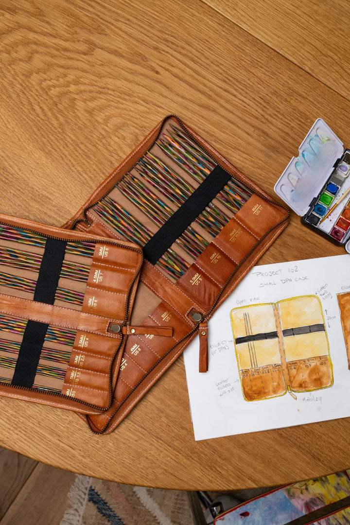Brown leather case with art supplies on a wooden surface