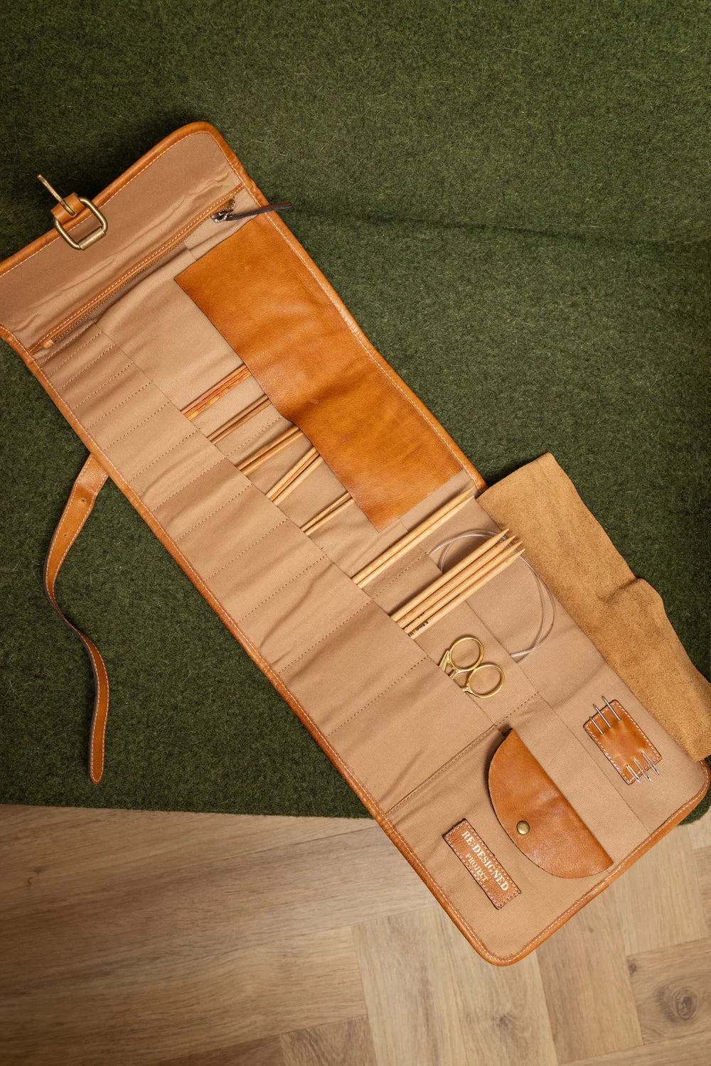 Open leather  needle case with tools on a green and wooden surface