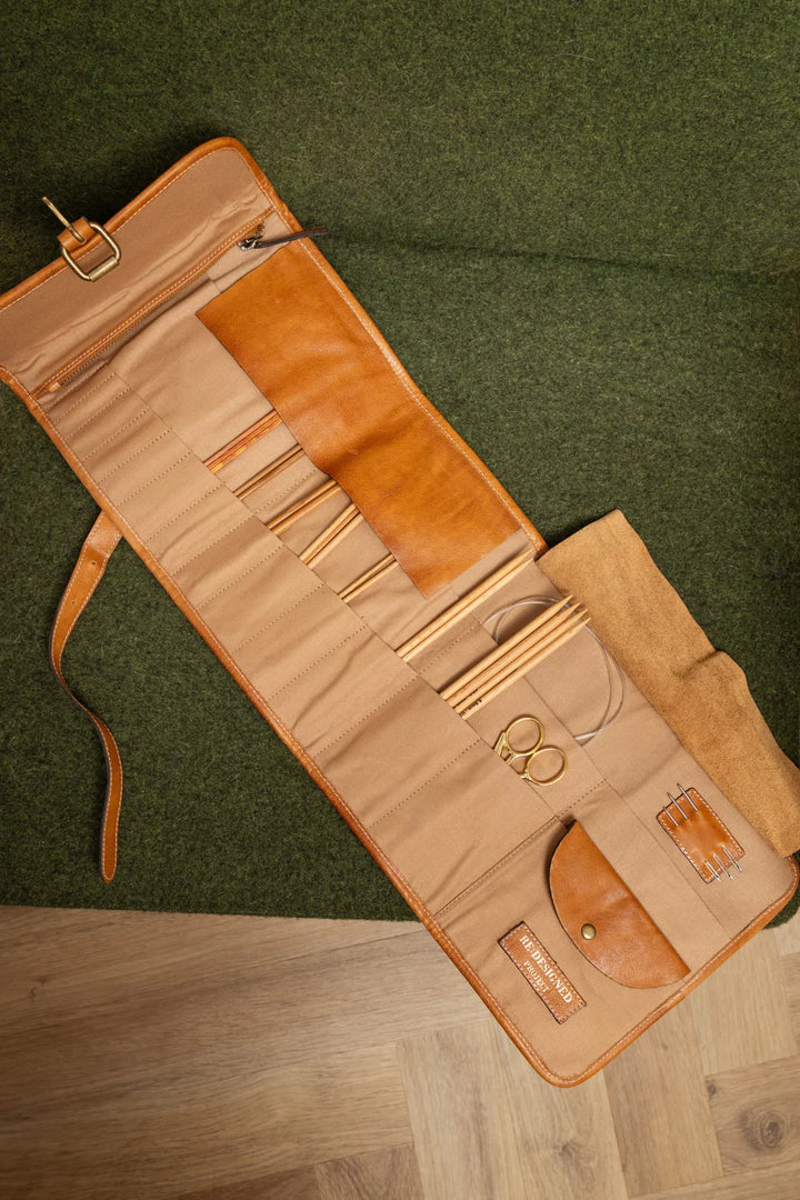 Open leather  needle case with tools on a green and wooden surface