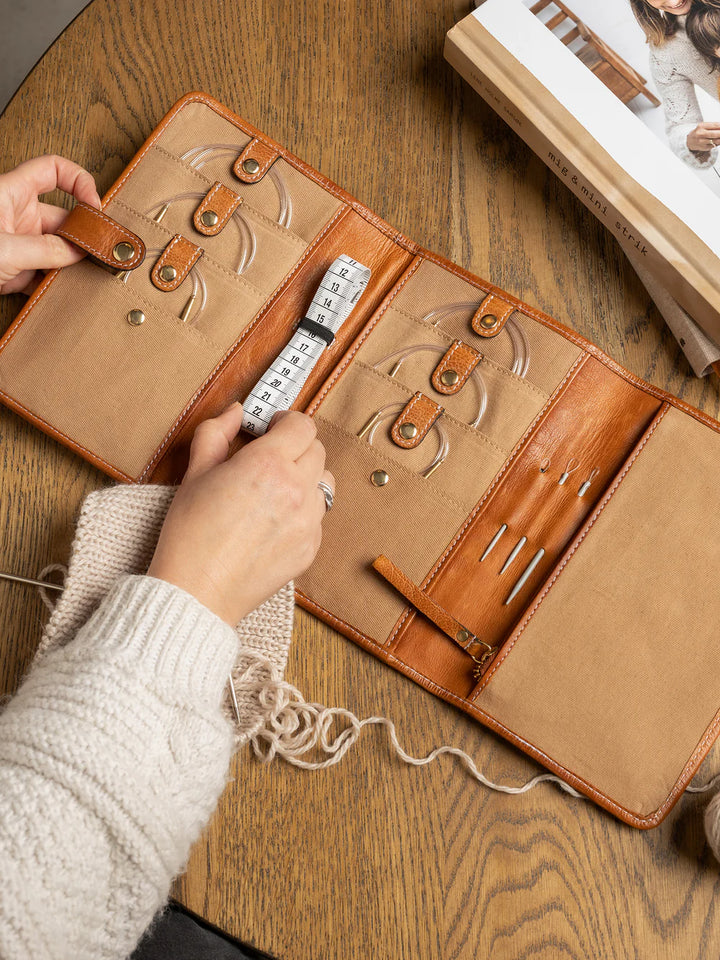 Brown leather needle case with embossed designs on a wooden surface