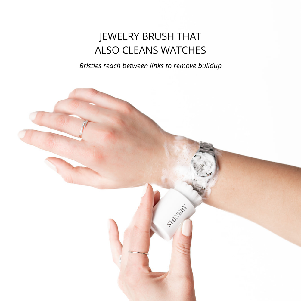 Person cleaning a watch with a jewelry brush on a white background