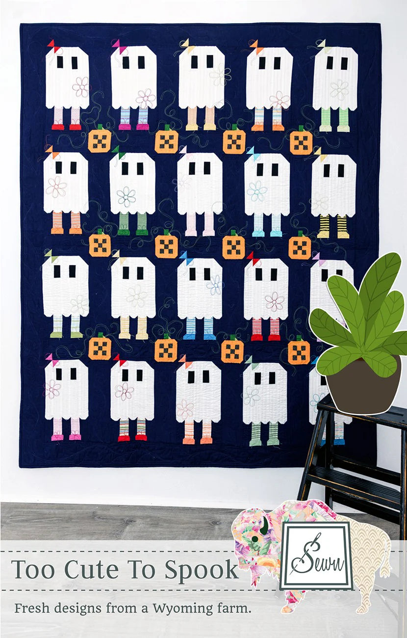 Decorative quilt with ghost pattern on a wall, featuring the brand 'Too Cute To Spook'.