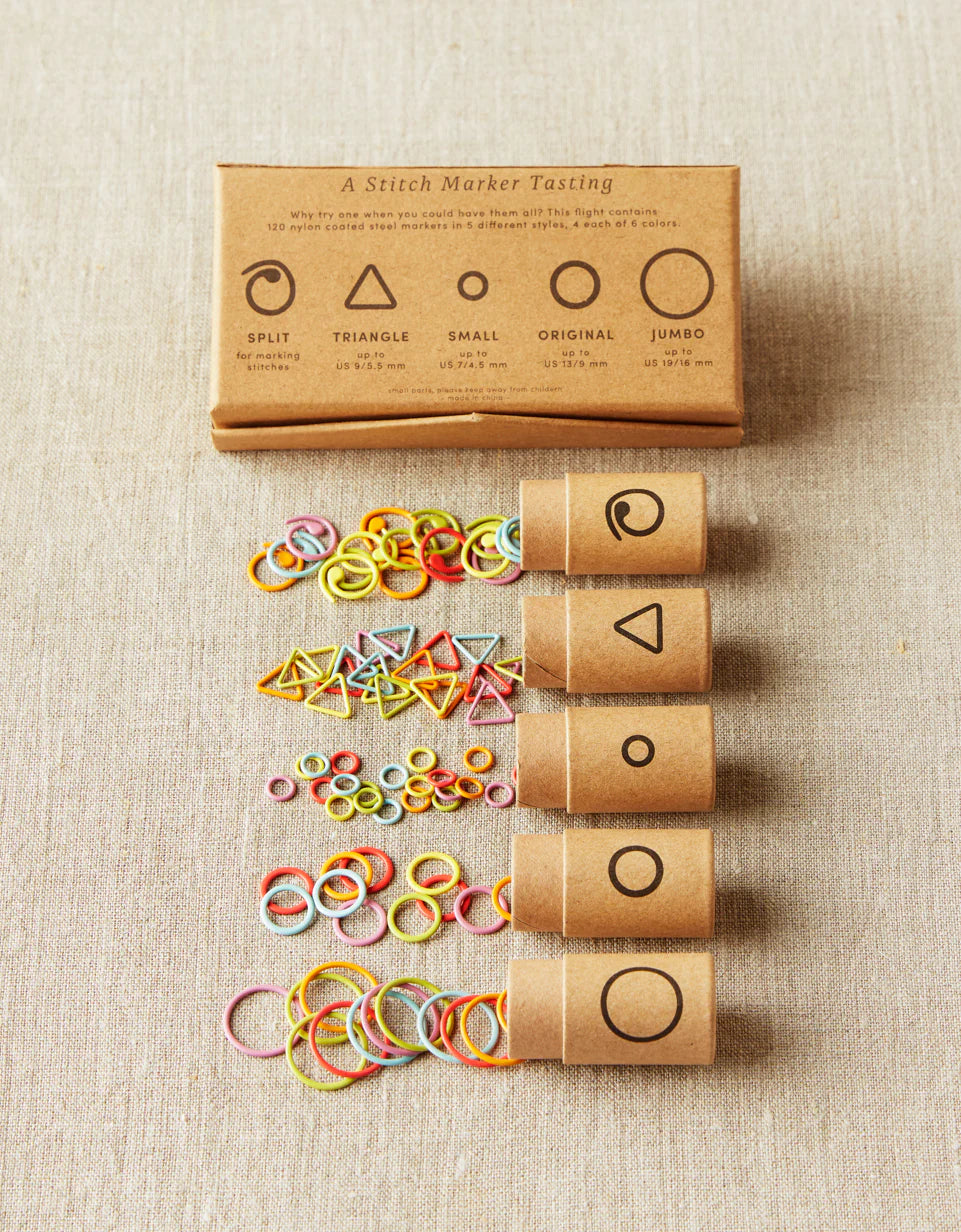 5 small cardboard tubes with plastic stitch markers in multiple bright colors. each tube contains a shape: large circle, medium circle, small circle, triangle, and split circle