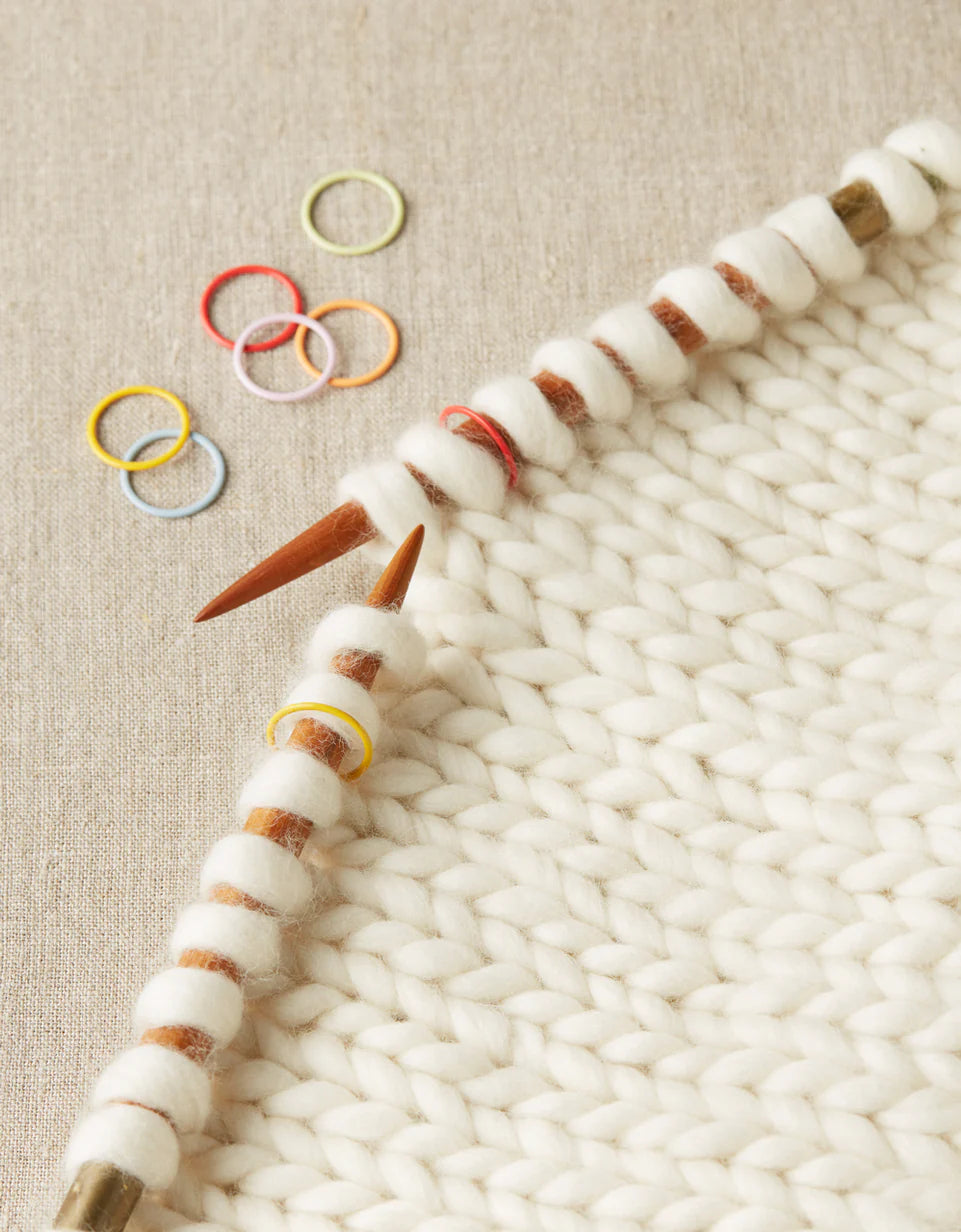 white knitted sample with needles showing stitch markers placed in between stitches on each needle