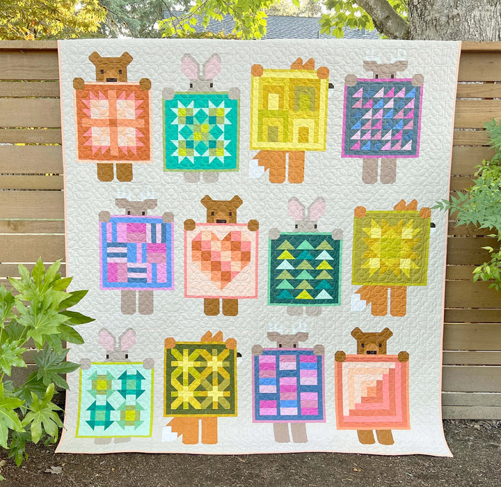 Quilt with teddy bear and rabbit designs holding various quilt blocks outdoors.