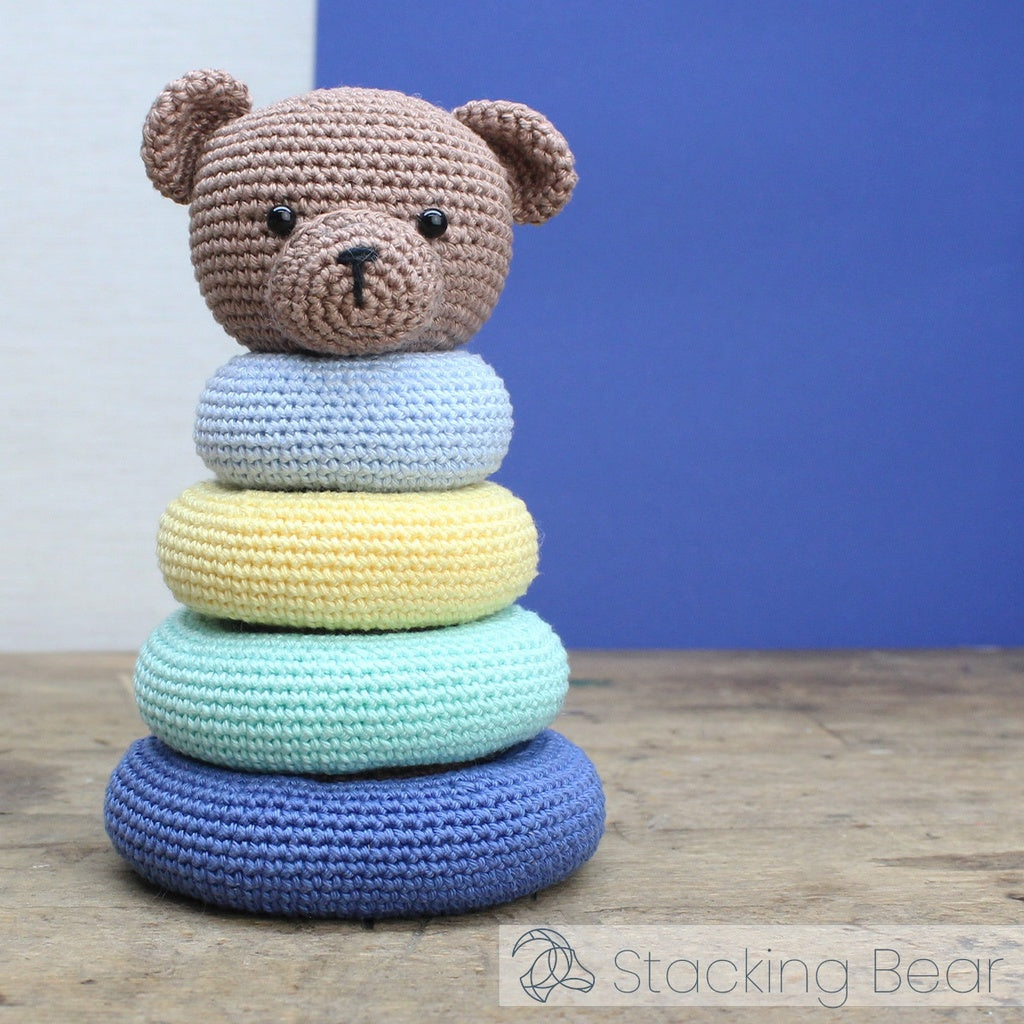 Stacking bear toy with colorful rings on a wooden surface against a blue wall.