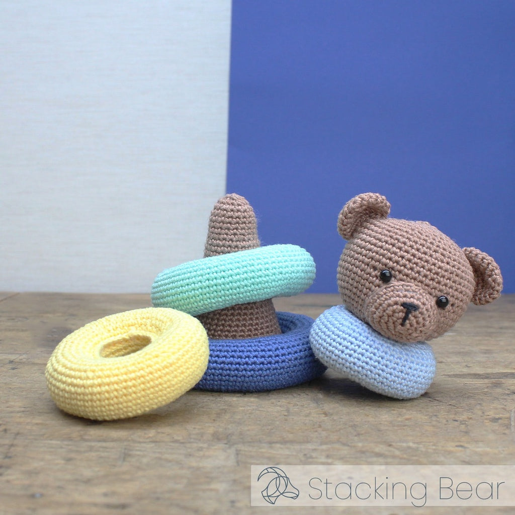Crocheted toys including a bear and rings on a wooden surface with a blue background.