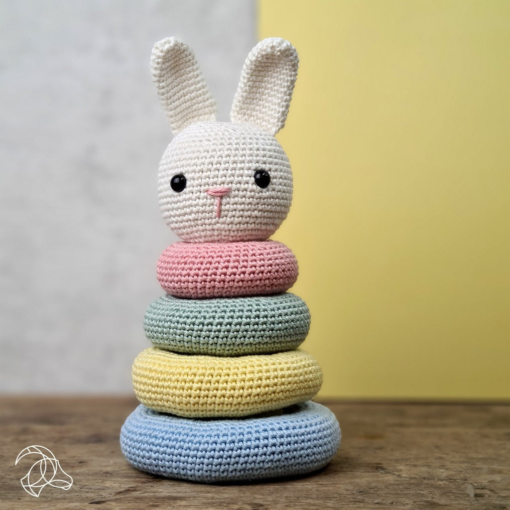 Crocheted stack of rings with a bunny design on a wooden surface against a neutral background