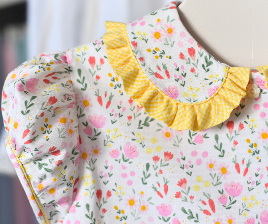 A floral patterned children's blouse with a Peter Pan collar, piping details, and a ruffle neckline.
