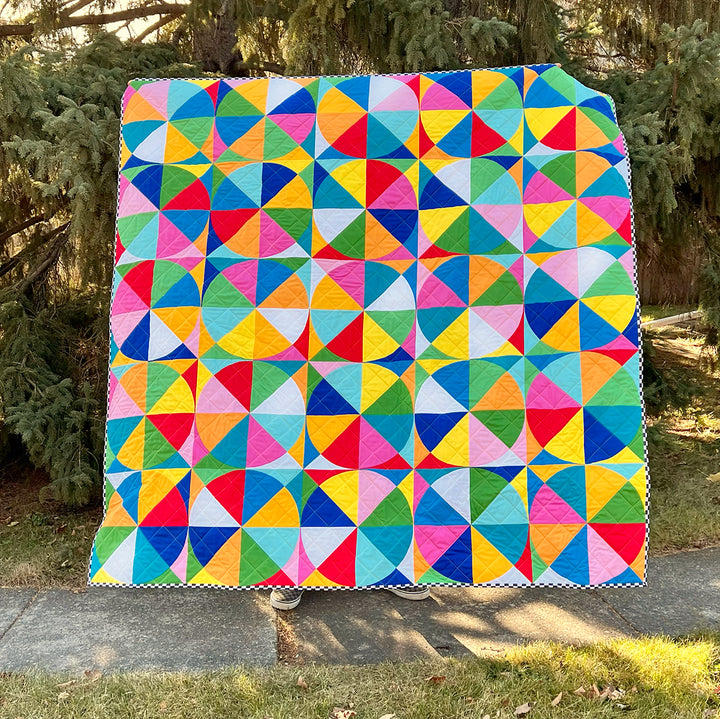 Colorful geometric quilt displayed outdoors with trees in the background