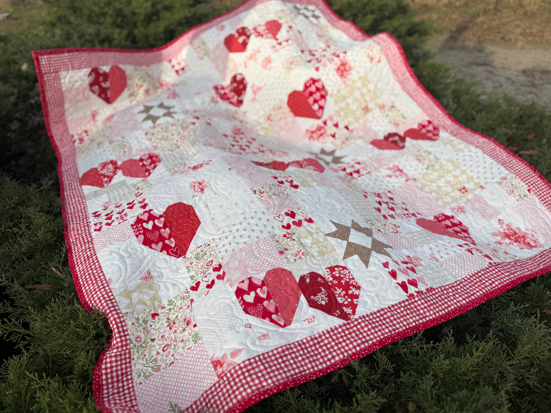 Quilt with red heart patterns on a grassy background