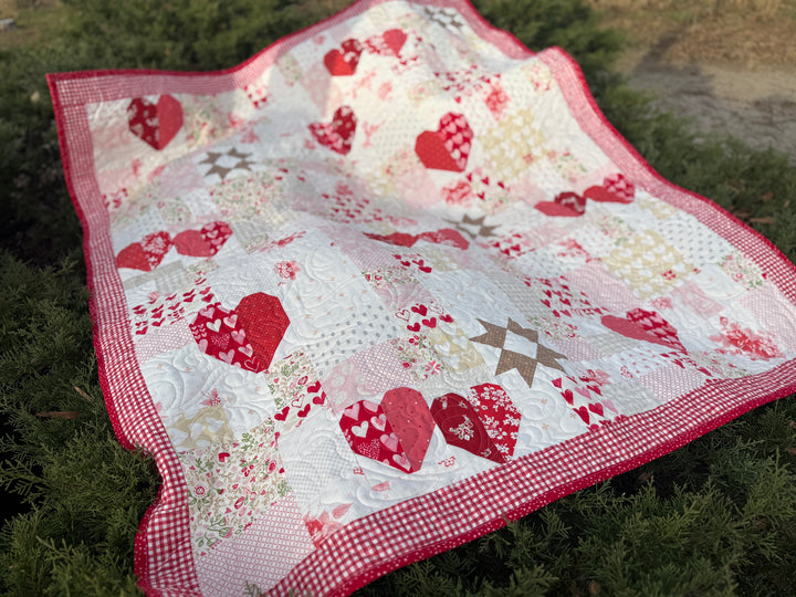 Quilt with red heart patterns on a grassy background