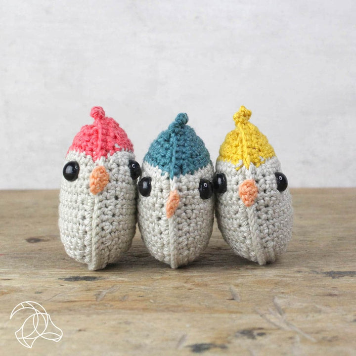 Three crochet birds with colorful hats on a wooden surface