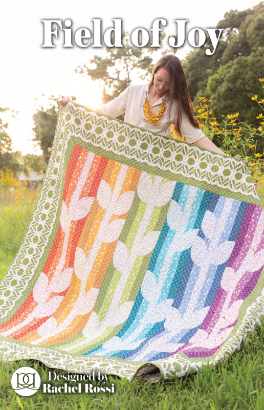 Woman holding a colorful quilt with floral patterns in a field