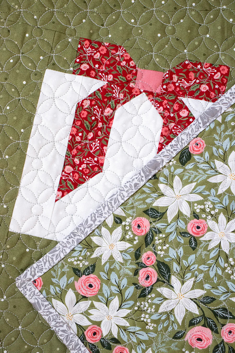 Quilted fabric with floral patterns and a red and white design on a green background