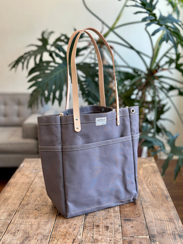 Gray tote bag with leather handles on a wooden table with plants in the background