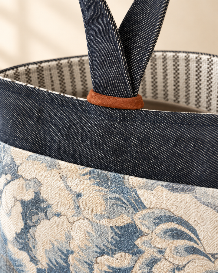 Close-up of a tote bag with dark navy woven handles, a dark navy top band, and a blue-and-cream floral patterned fabric body.