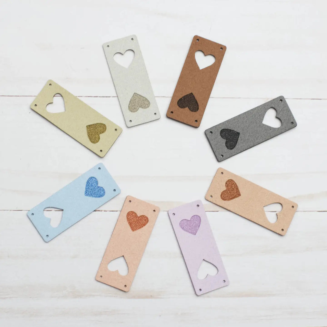 Decorative heart-shaped cutouts on colorful rectangular leather tags arranged on a white wooden surface.