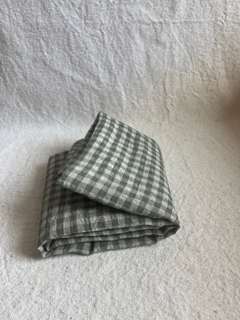 Medium green colored gingham folded in half on a khaki colored background. 