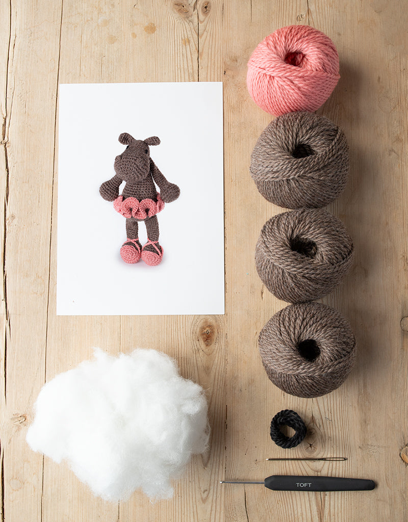 animal card, poly stuffing, balls of yarn, darning needle, and a crochet hook lying on a wooden table