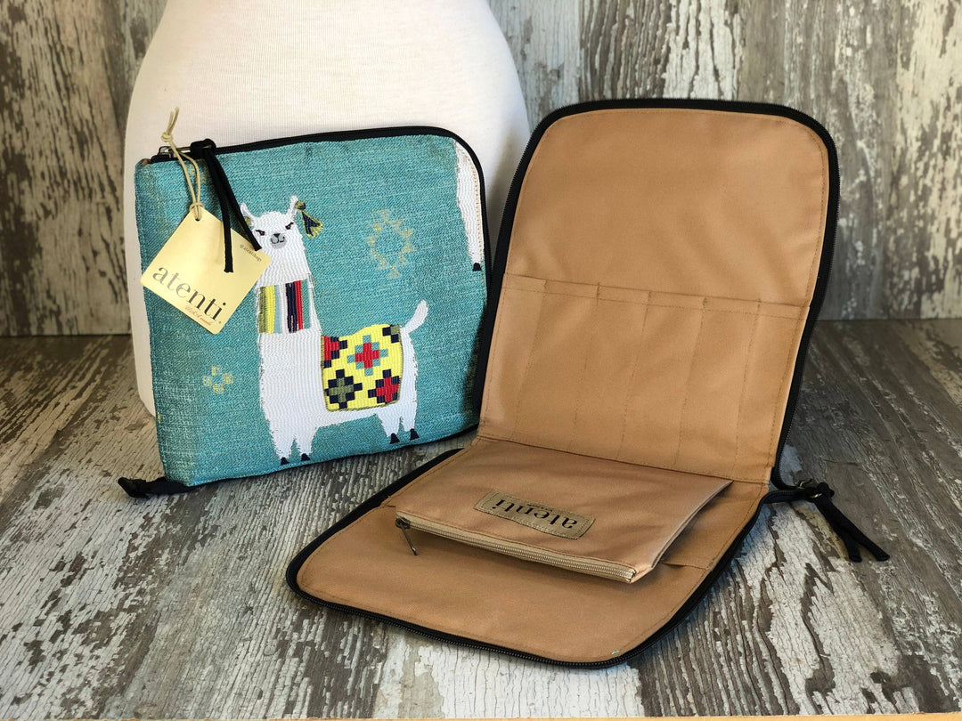 A turquoise woven pouch with a white llama and colorful patterned scarf, shown next to an open tan zippered sleeve with black trim. A small tag on the pouch reads 'HURRIC'.