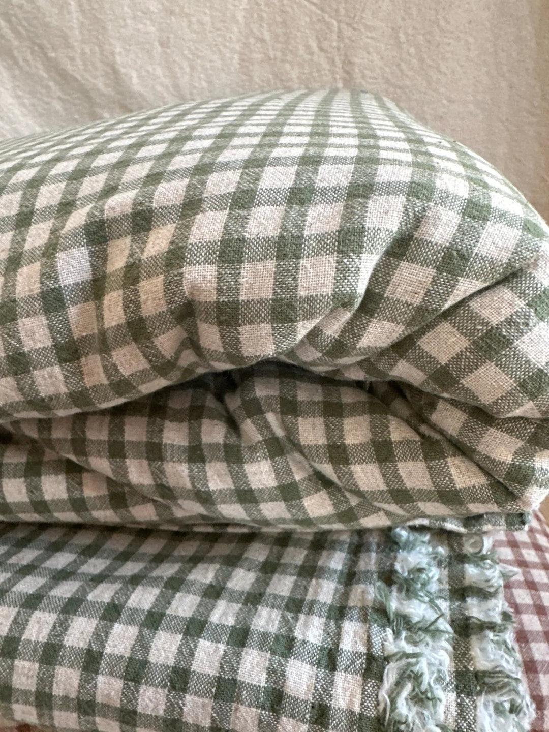 Green gingham fabric folded in half resting on top of more green gingham fabric against a tan background. 