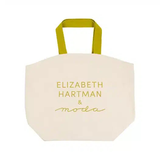 Beige tote bag with yellow handles and gold text on a white background