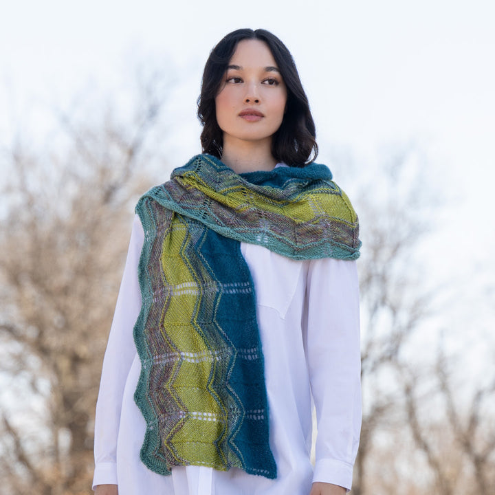 Woman wearing a green and blue patterned scarf against a blurred natural background