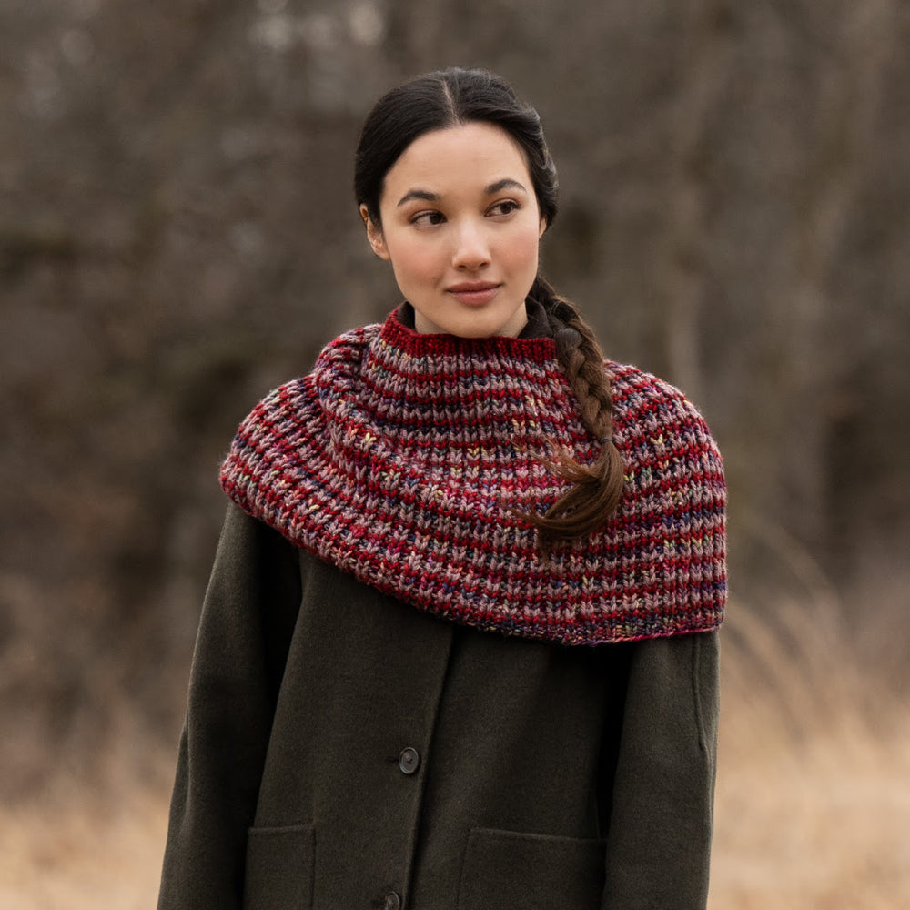 Woman wearing a dark coat and a colorful knitted cowl against a blurred natural background