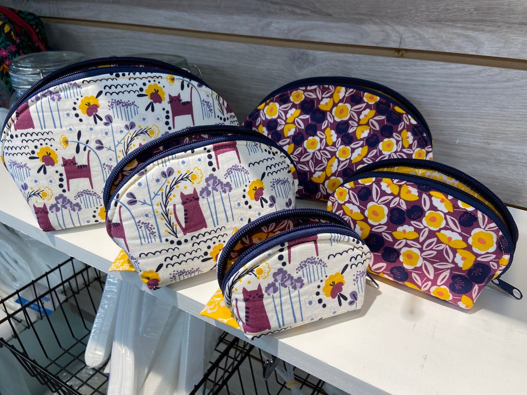 A collection of handmade zipper pouches with floral and geometric patterns, displayed on a metal rack.